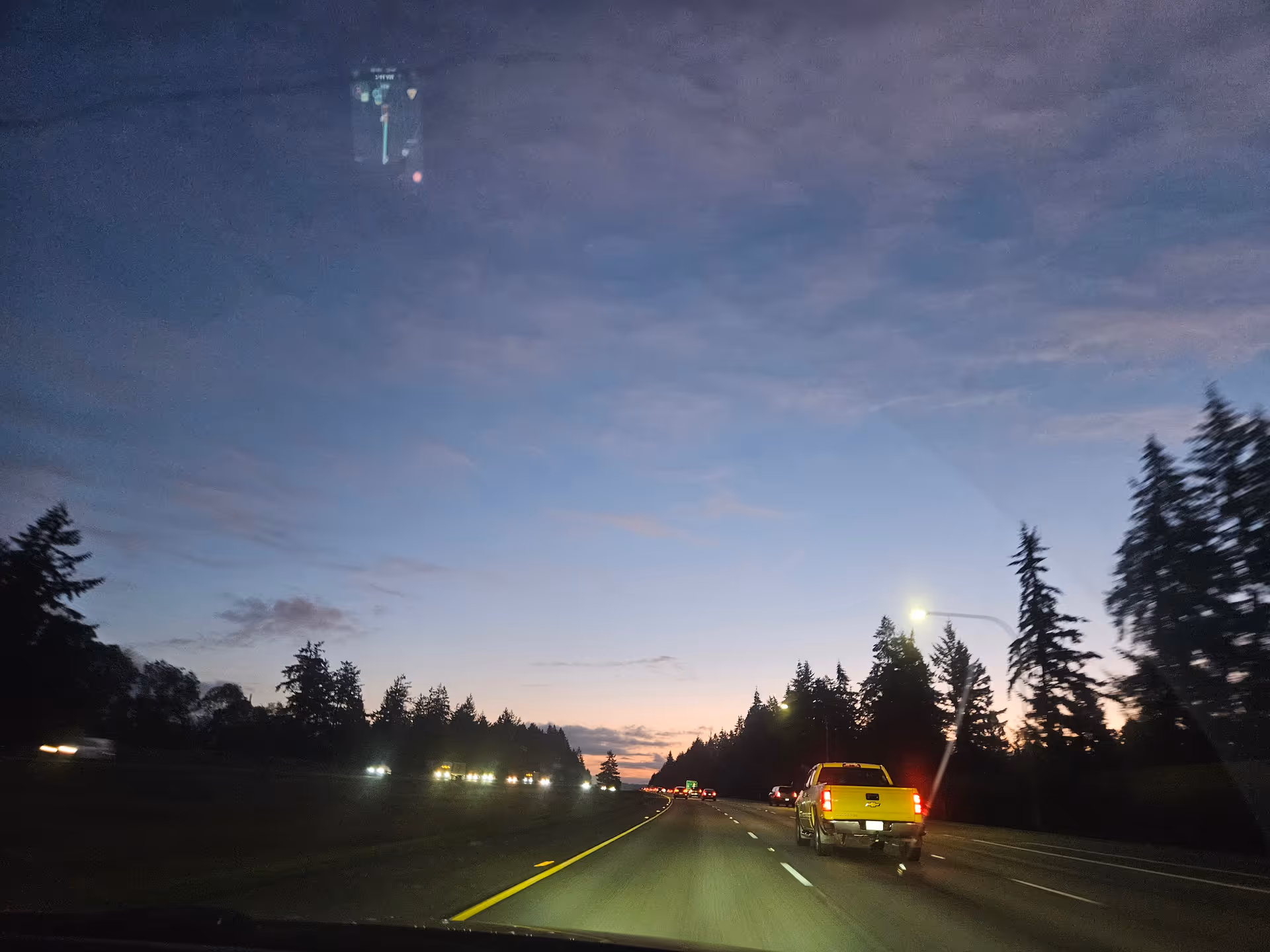 Dusk highway scene with trees on both sides and a fading sunset.