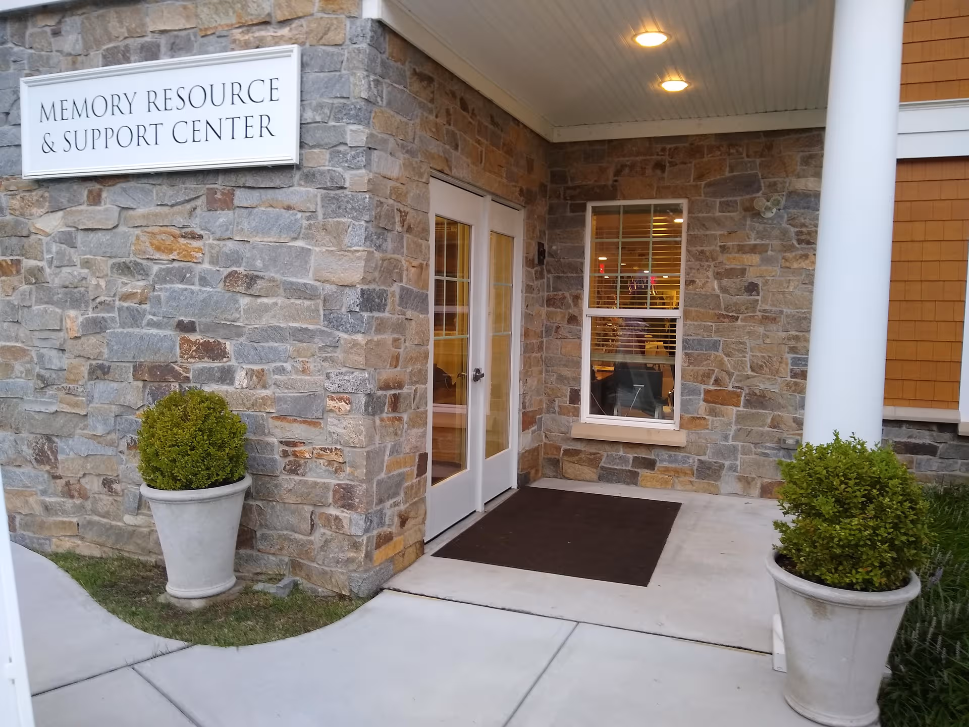 Stone facade entrance of Maplewood at Stony Hill with sign, door, window, and planters.