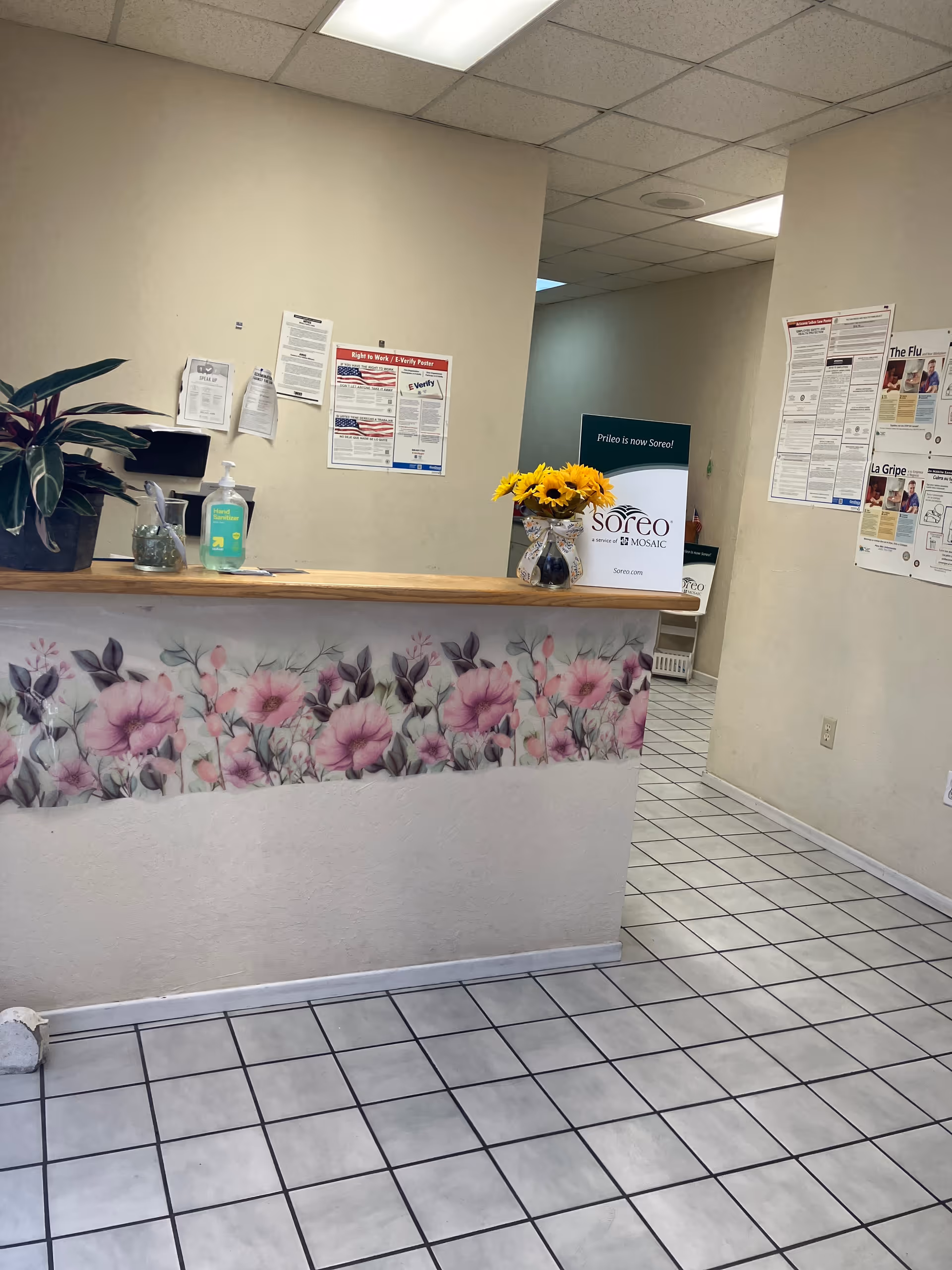 Reception area with floral counter, plants, and sunflower bouquet inside a senior living facility.