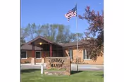 Exterior of Select Senior Living II with flag, trees, and a lawn sign.