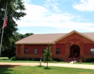 Front exterior of Enon Country Manor, a red brick senior living facility with flagpole and lawn.