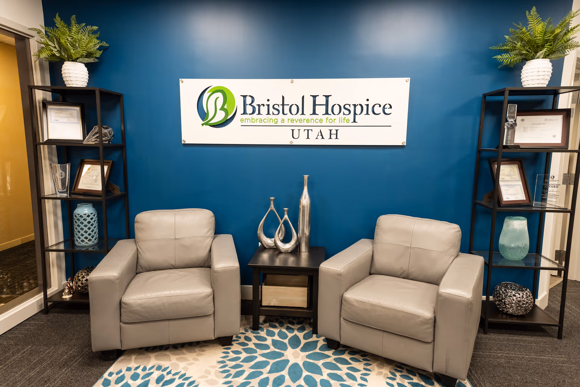 Two gray armchairs flank a small table in a blue-walled Bristol Hospice lobby.