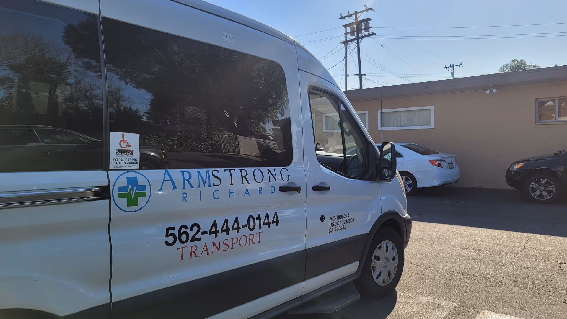 White Armstrong Richard Transport van with wheelchair sticker parked beside a beige building.