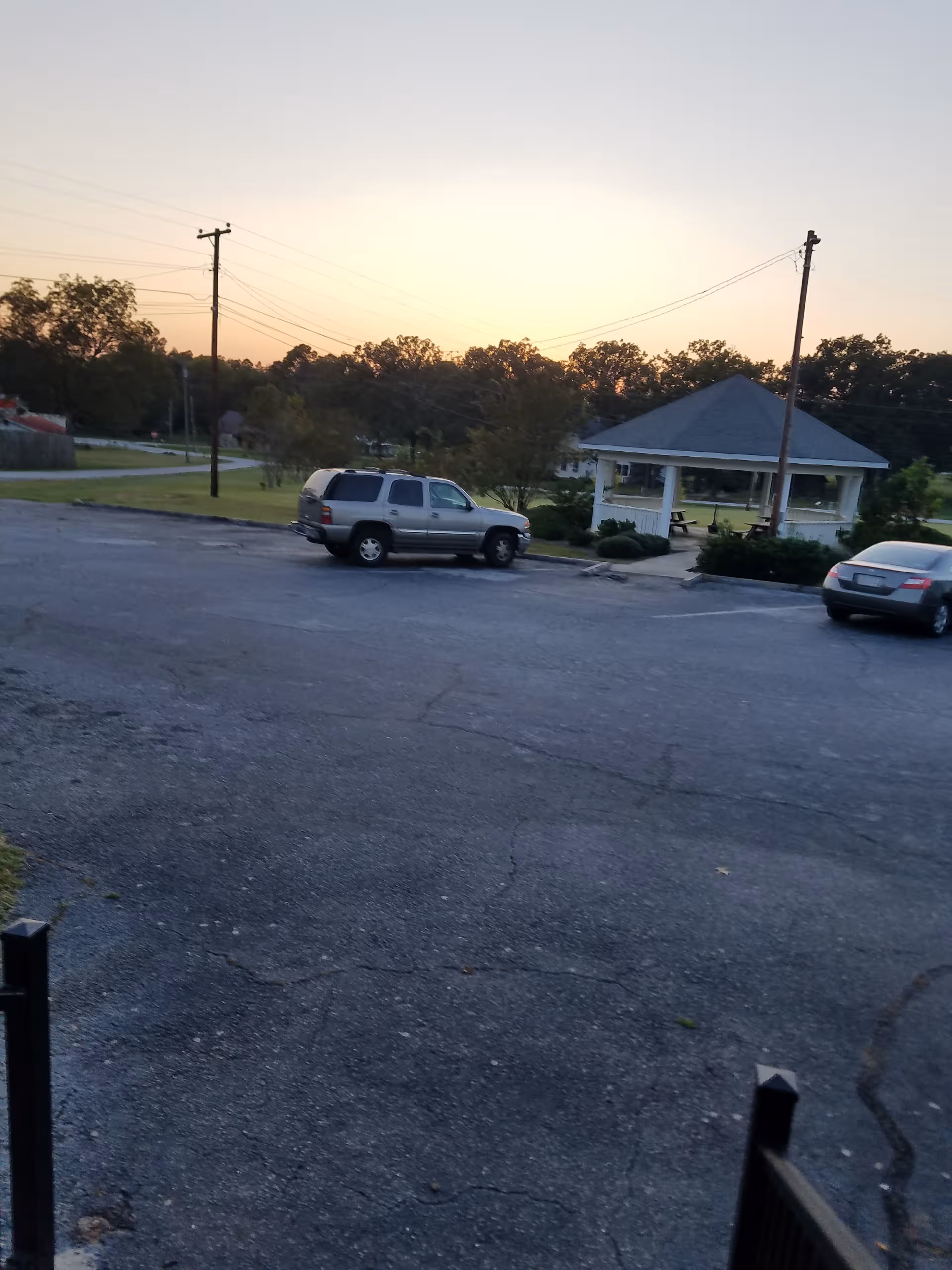 Sunset over a parking lot with a gazebo and distant trees.