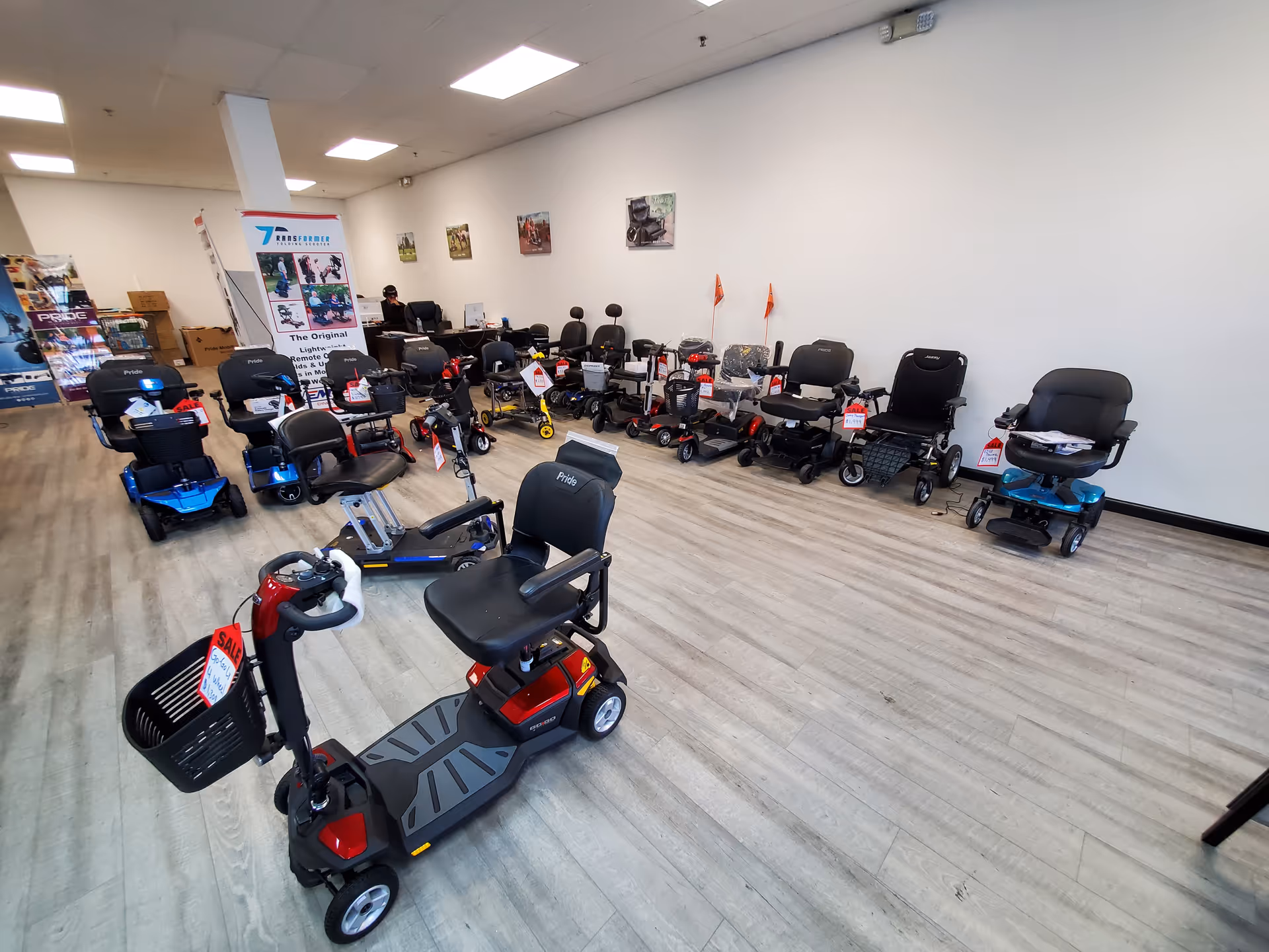Indoor showroom with numerous mobility scooters and chairs arranged along white walls.