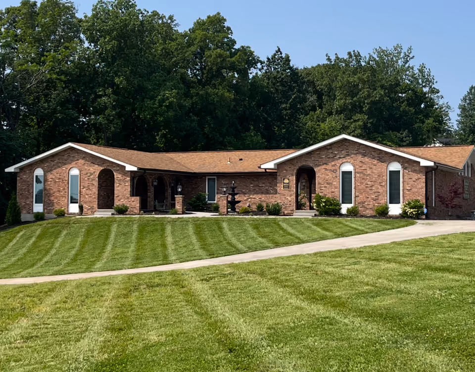 Brick senior living facility with arched doorways and a well-manicured lawn in front.