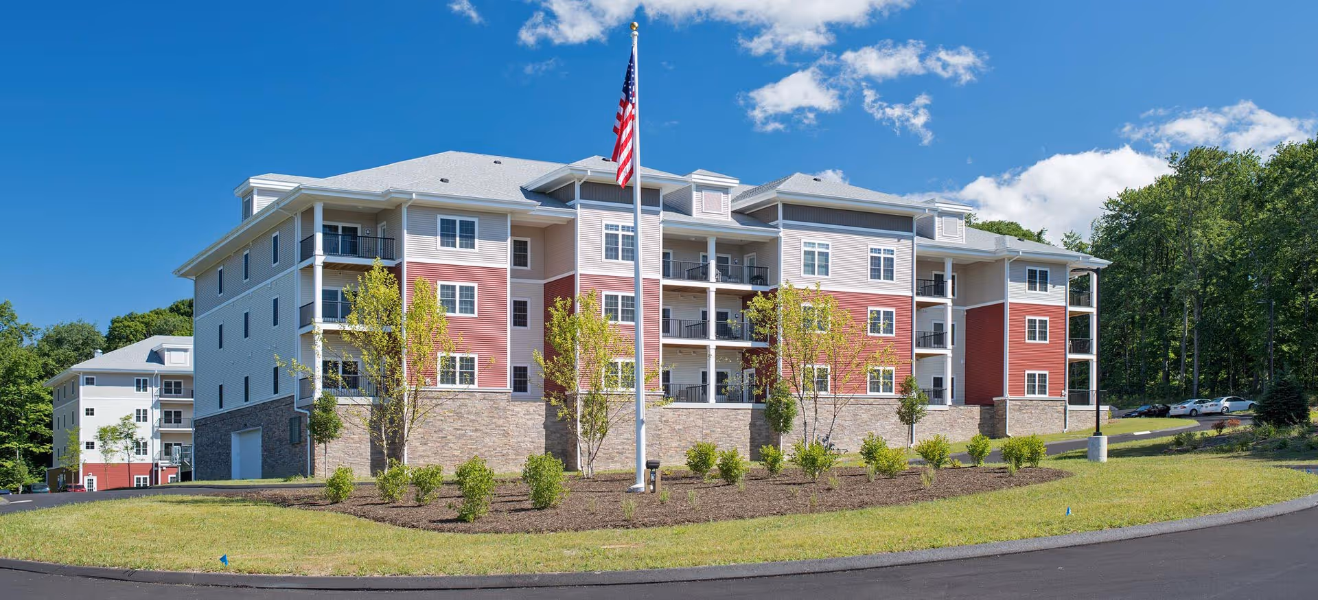 Exterior view of a multi-story senior living building with landscaping and American flag.