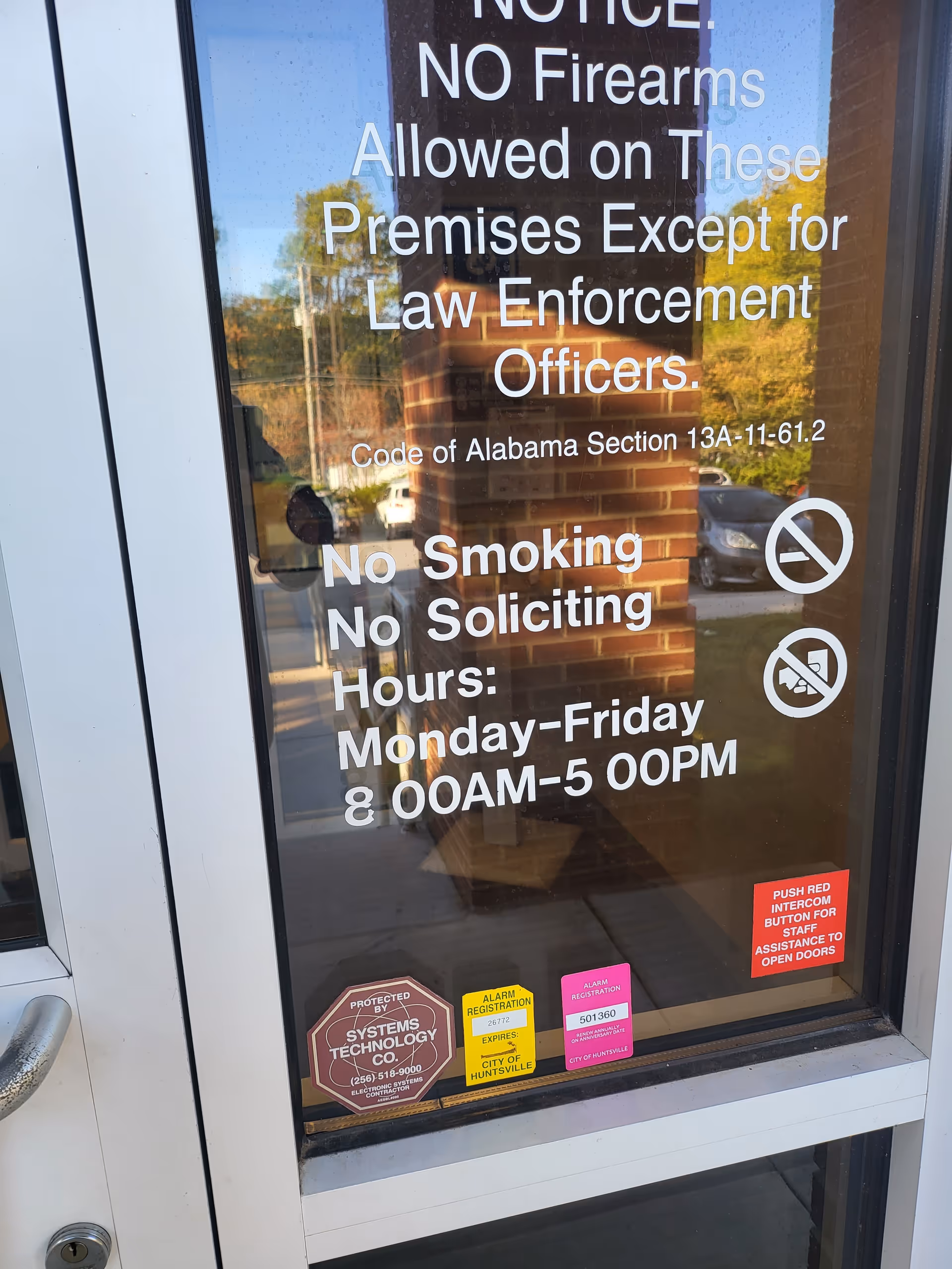 Glass entrance door covered with notices: no firearms, no smoking, no soliciting, hours.