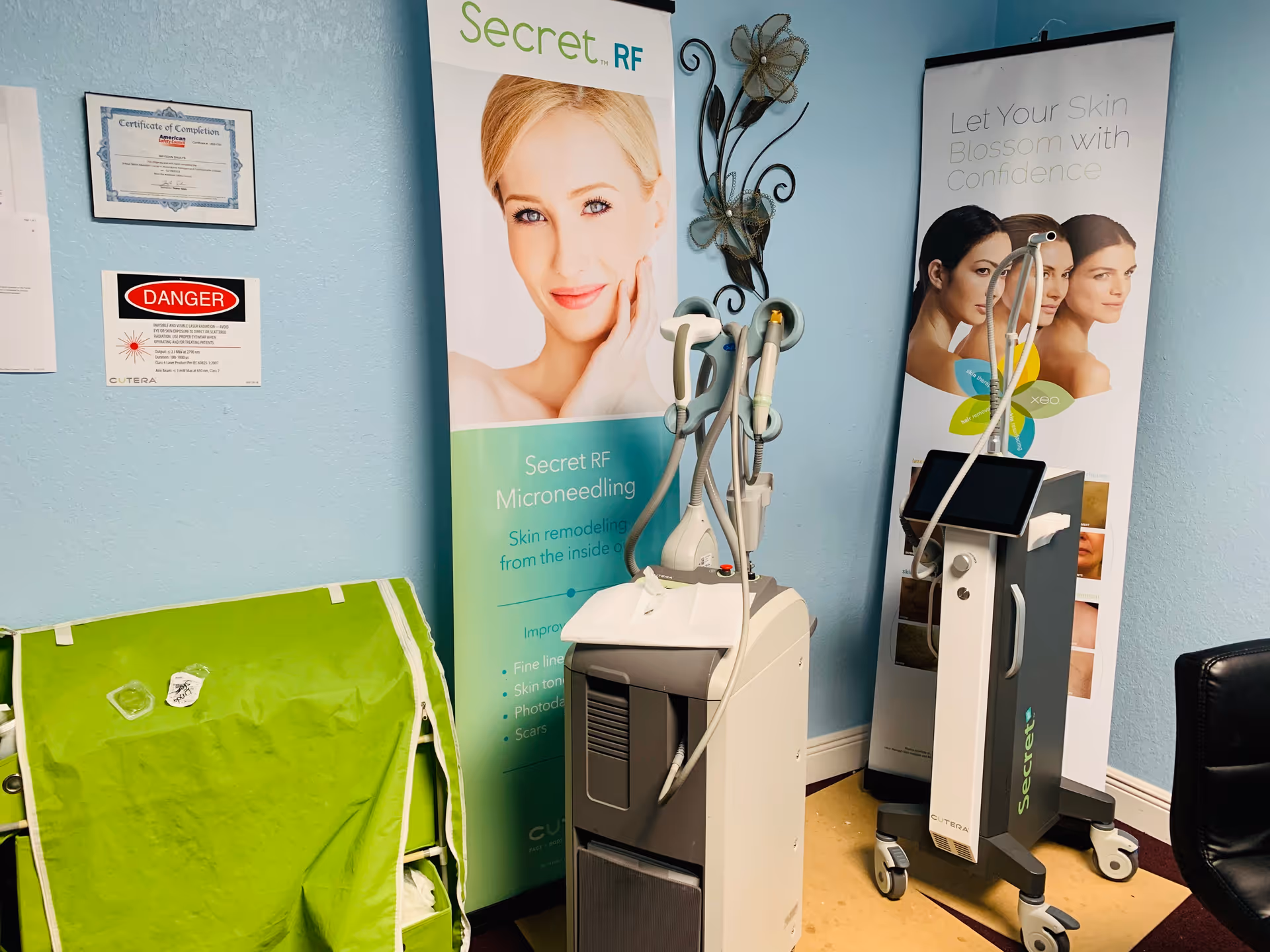 Treatment room with aesthetic medical devices and promotional banners against blue walls.