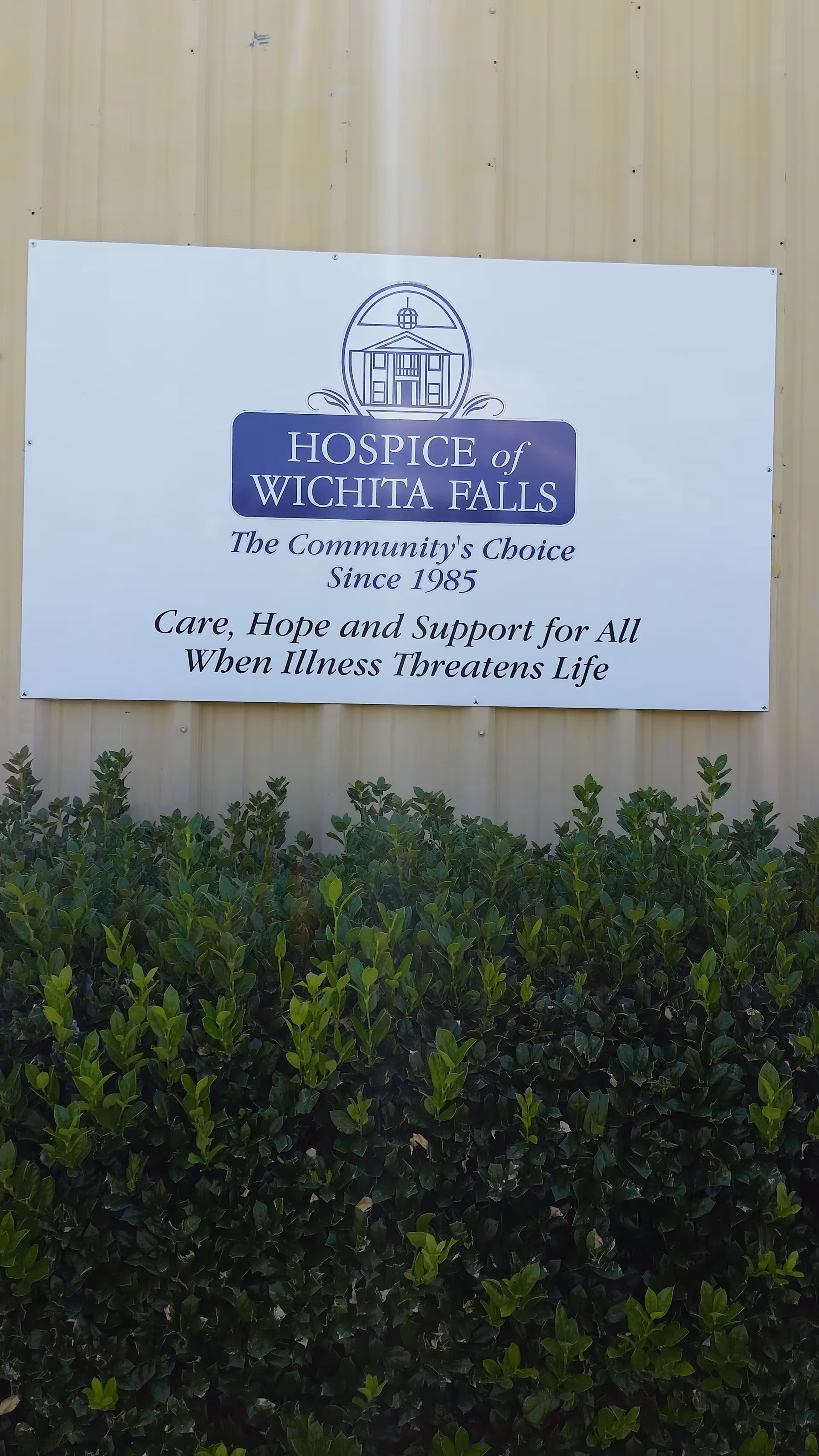 Exterior wall featuring Hospice of Wichita Falls Vernon Office sign with shrubs in front