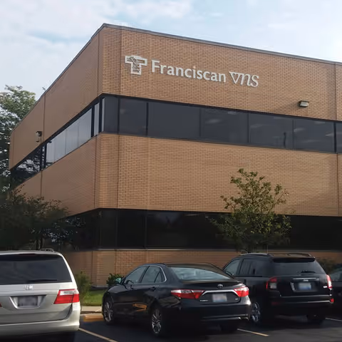 Brick exterior building with Franciscan VNS Home Care sign and parked cars.