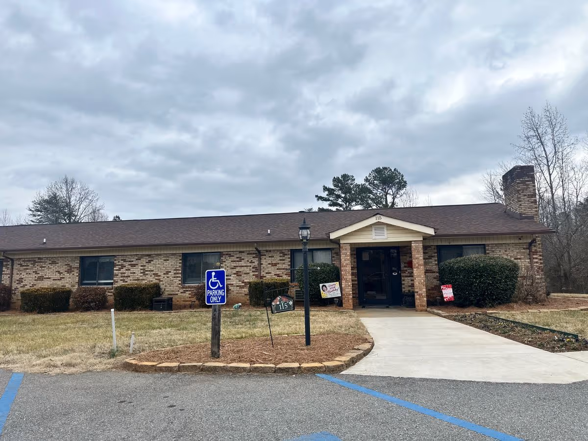 Front exterior of a single-story brick senior living building with a walkway, lamp post, and a handicap parking sign.