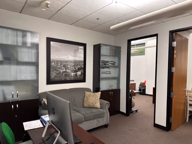 Office-like reception area with gray sofa, desk, monitor, and glass-front cabinets.