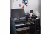 Desk computer workstation with monitor, keyboard, papers, and small electronics in a compact room.