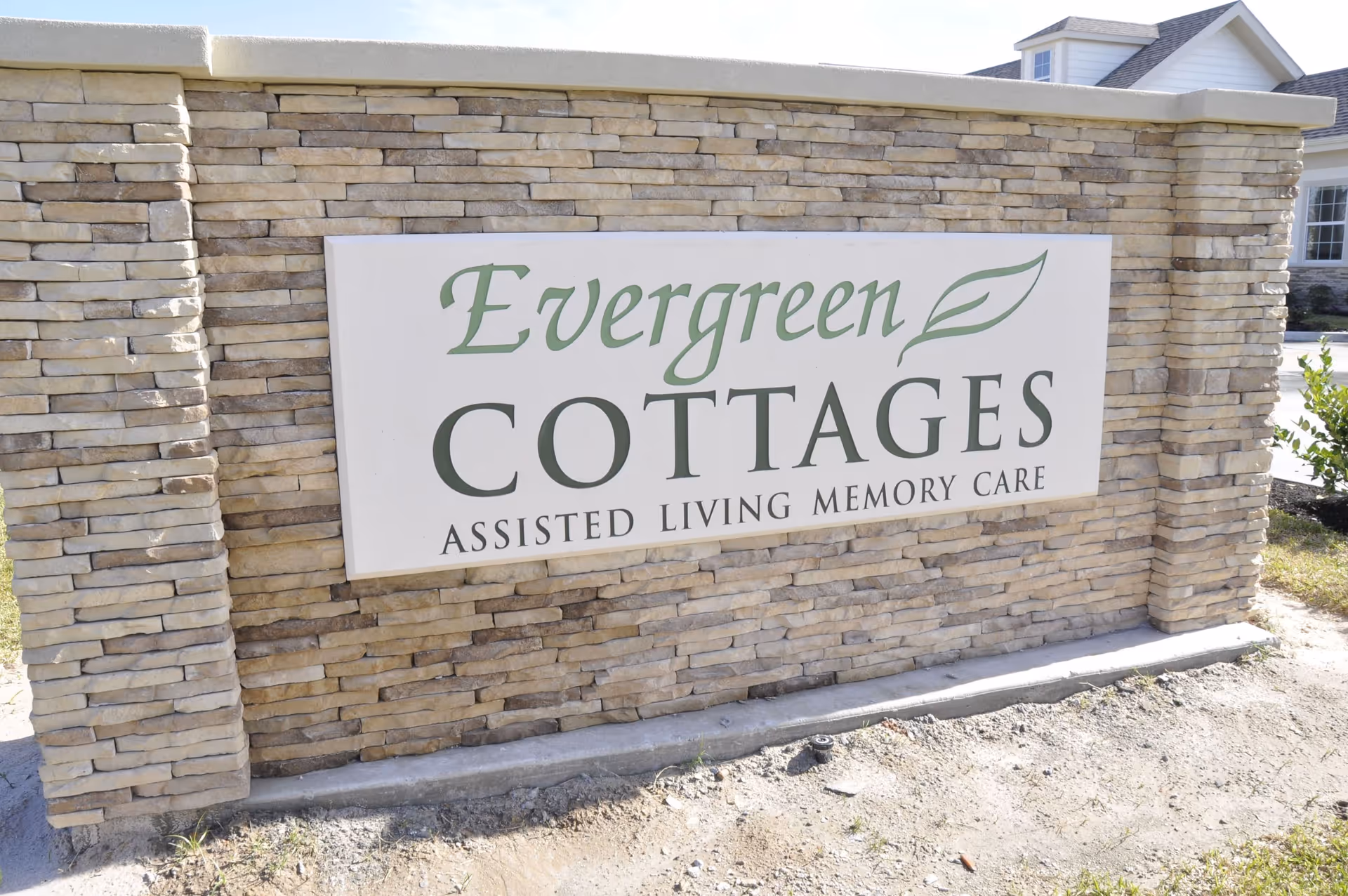 Stone sign on a stone wall reads Evergreen Cottages at entrance.