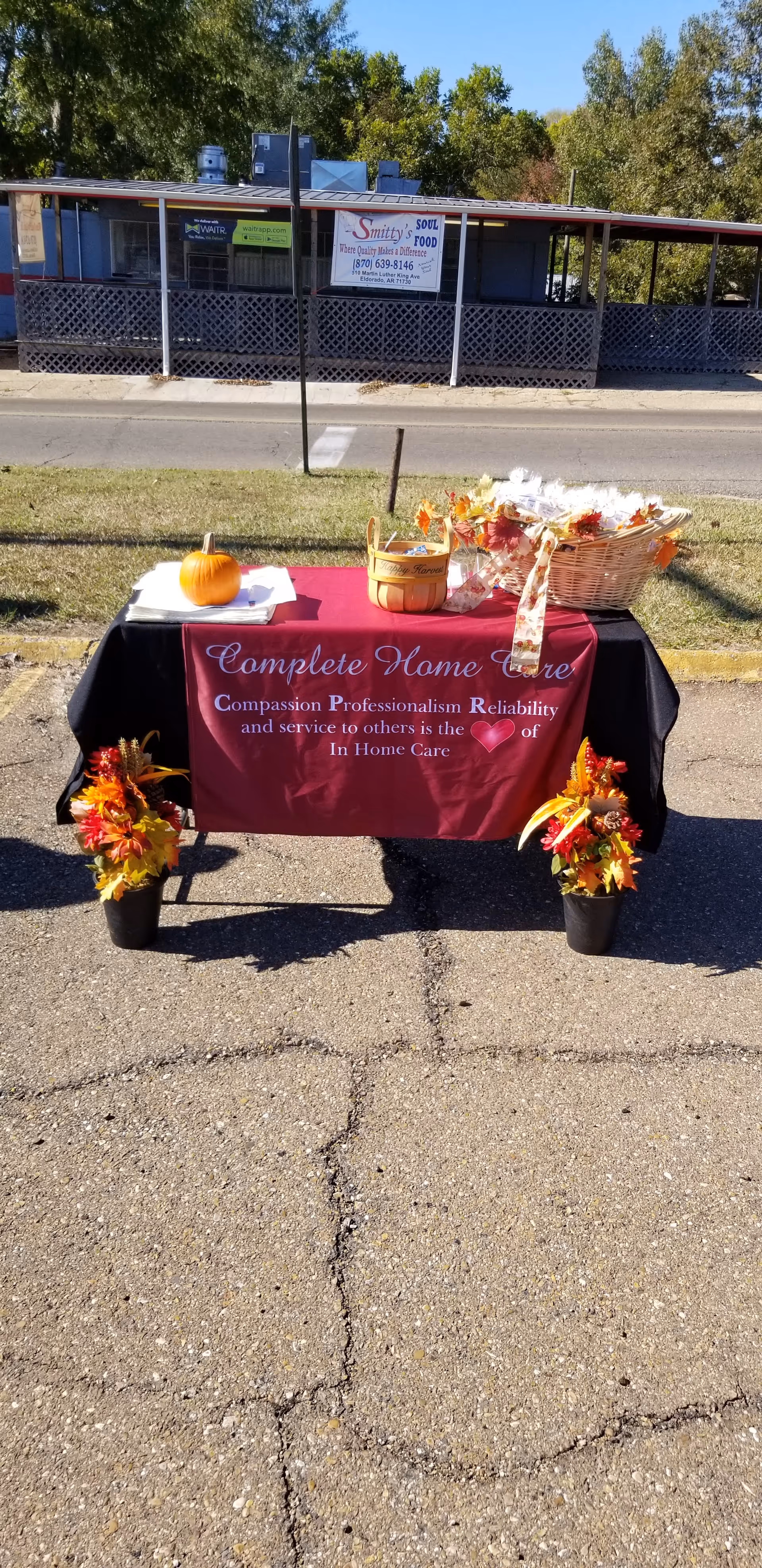 Outdoor display table with burgundy Complete Home Care banner and autumn decor.