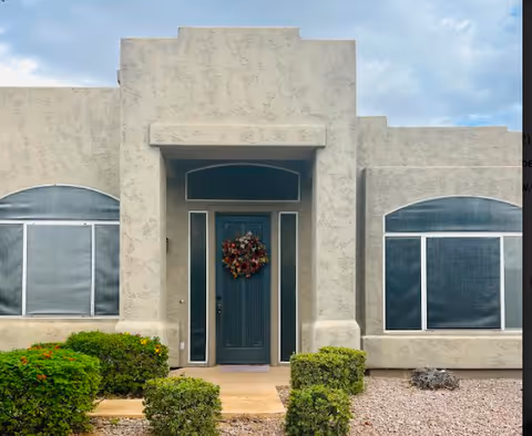 Beige building front with teal door, wreath, and trimmed shrubs.