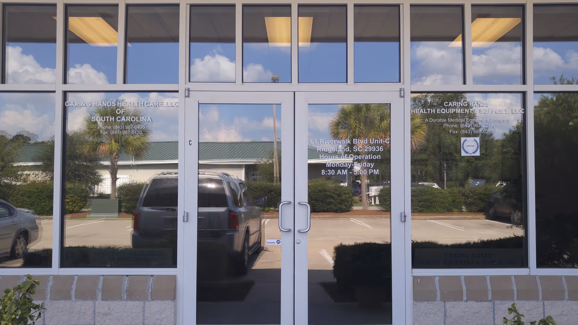 Glass front doors reflect the parking lot and Caring Hands Health Care signage.