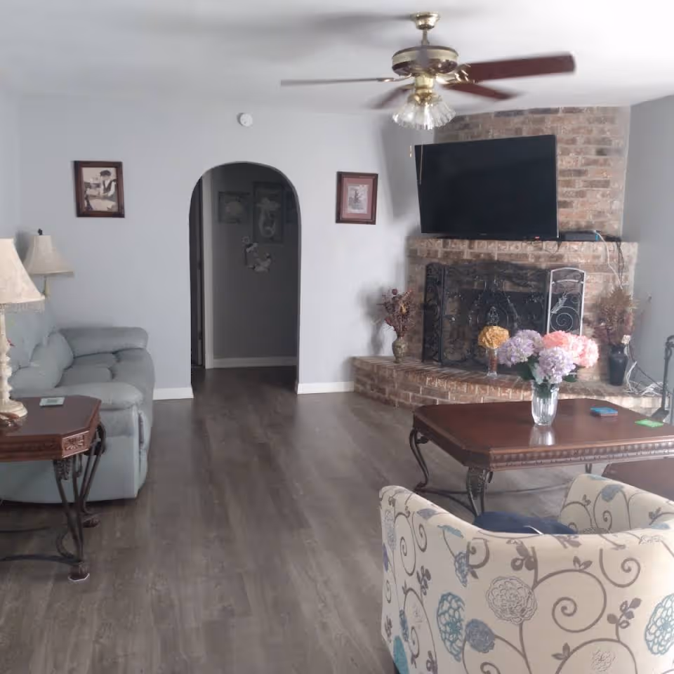 Living room in The New Horizon senior facility with brick fireplace, TV, ceiling fan, and seating.