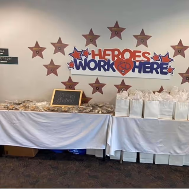 Indoor event setup with a 'Heroes Work Here' banner and gift bags on tables.