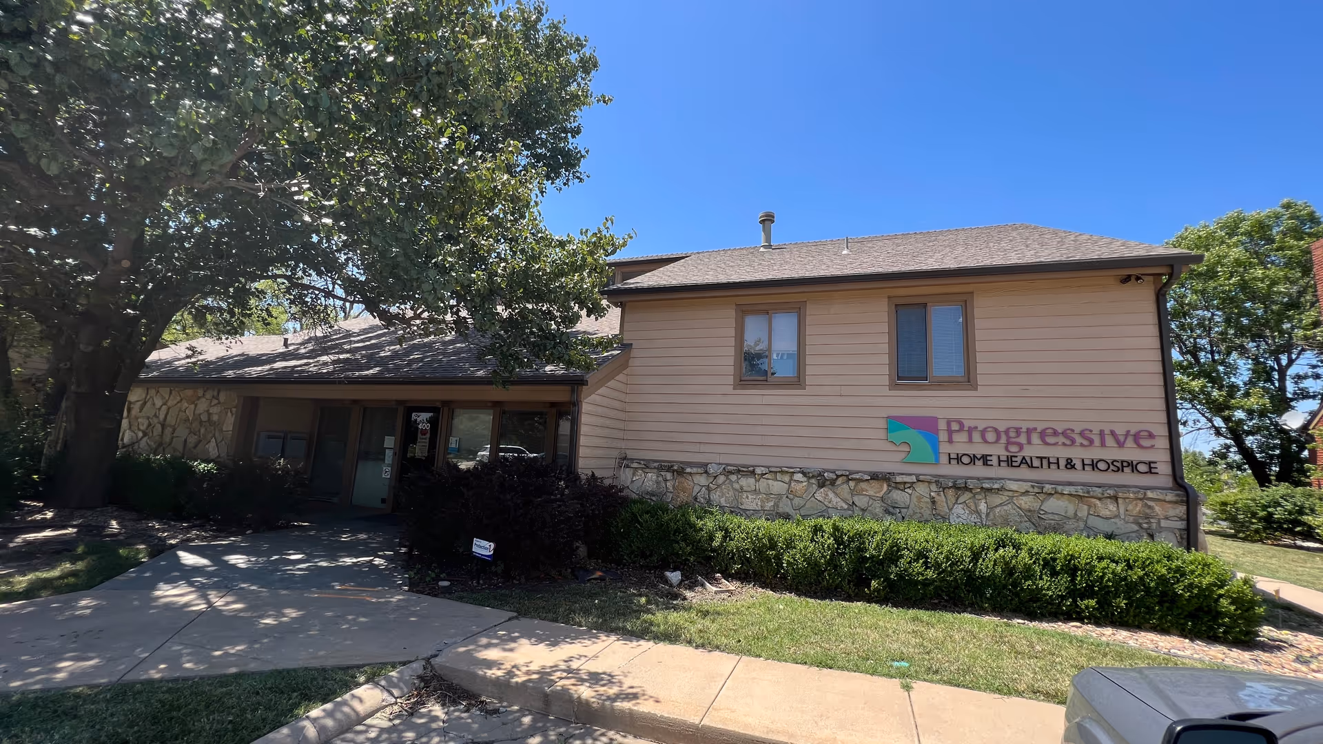 Exterior view of Progressive Home Health & Hospice building with sign, trees, and blue sky