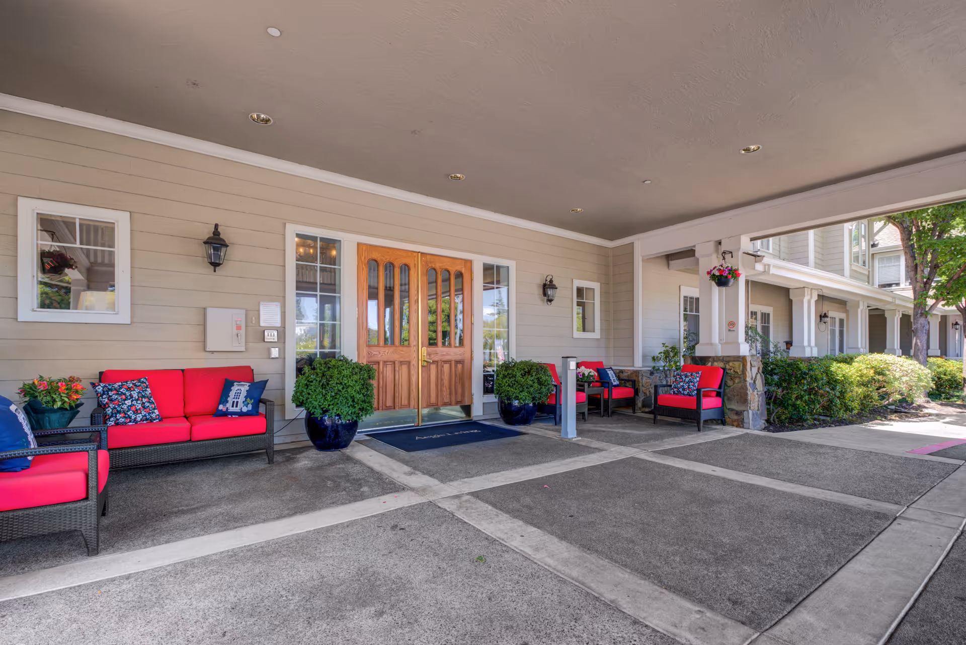 Covered entrance/porte-cochere with red-cushioned outdoor seating, potted plants, and wooden double doors.