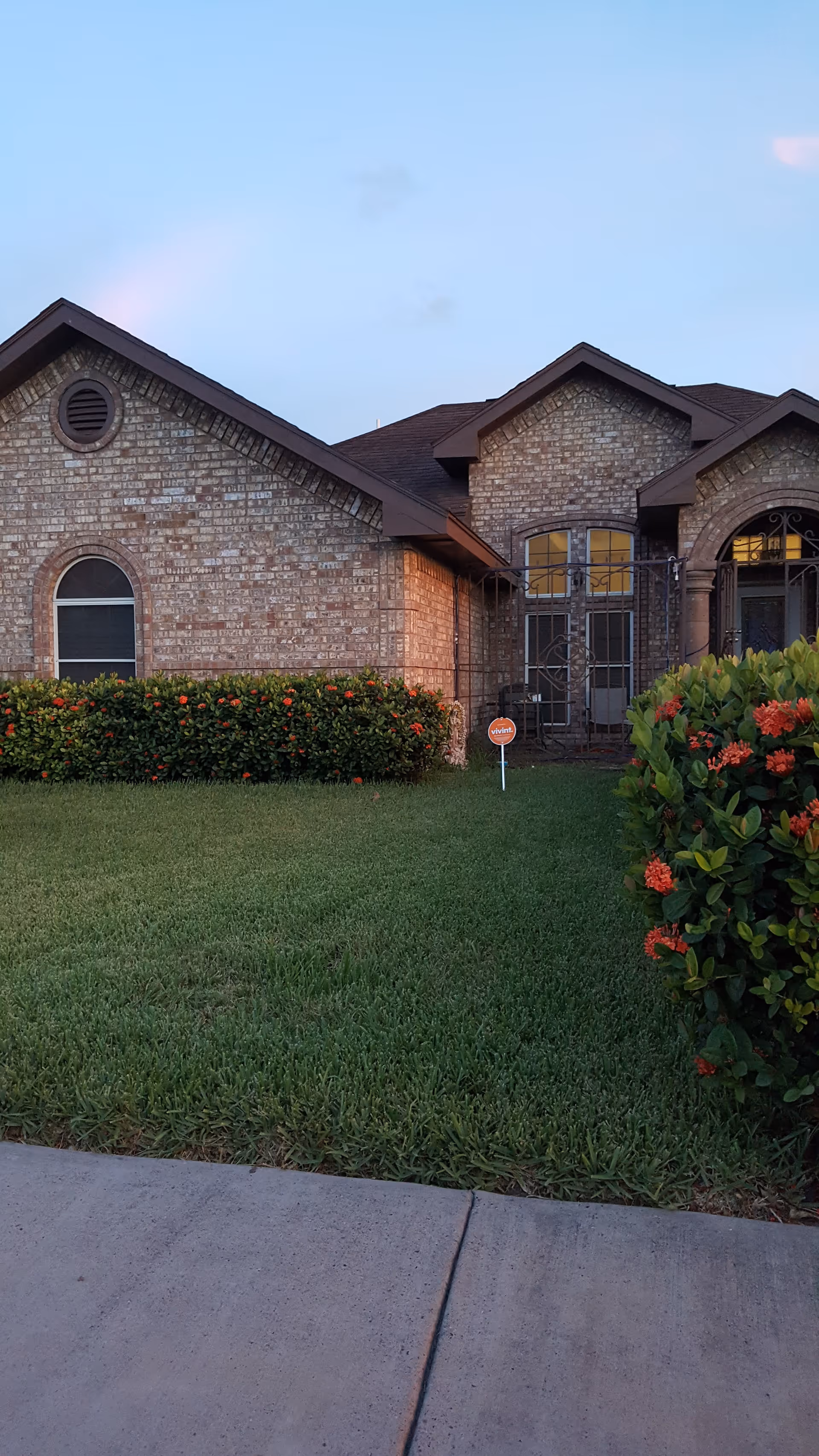 Brick senior living facility exterior with manicured lawn, shrubs, and a concrete sidewalk.
