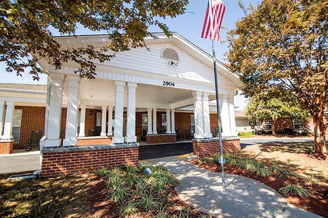 Front entrance of The Pearl of the Shoals senior living facility with columns and flag.