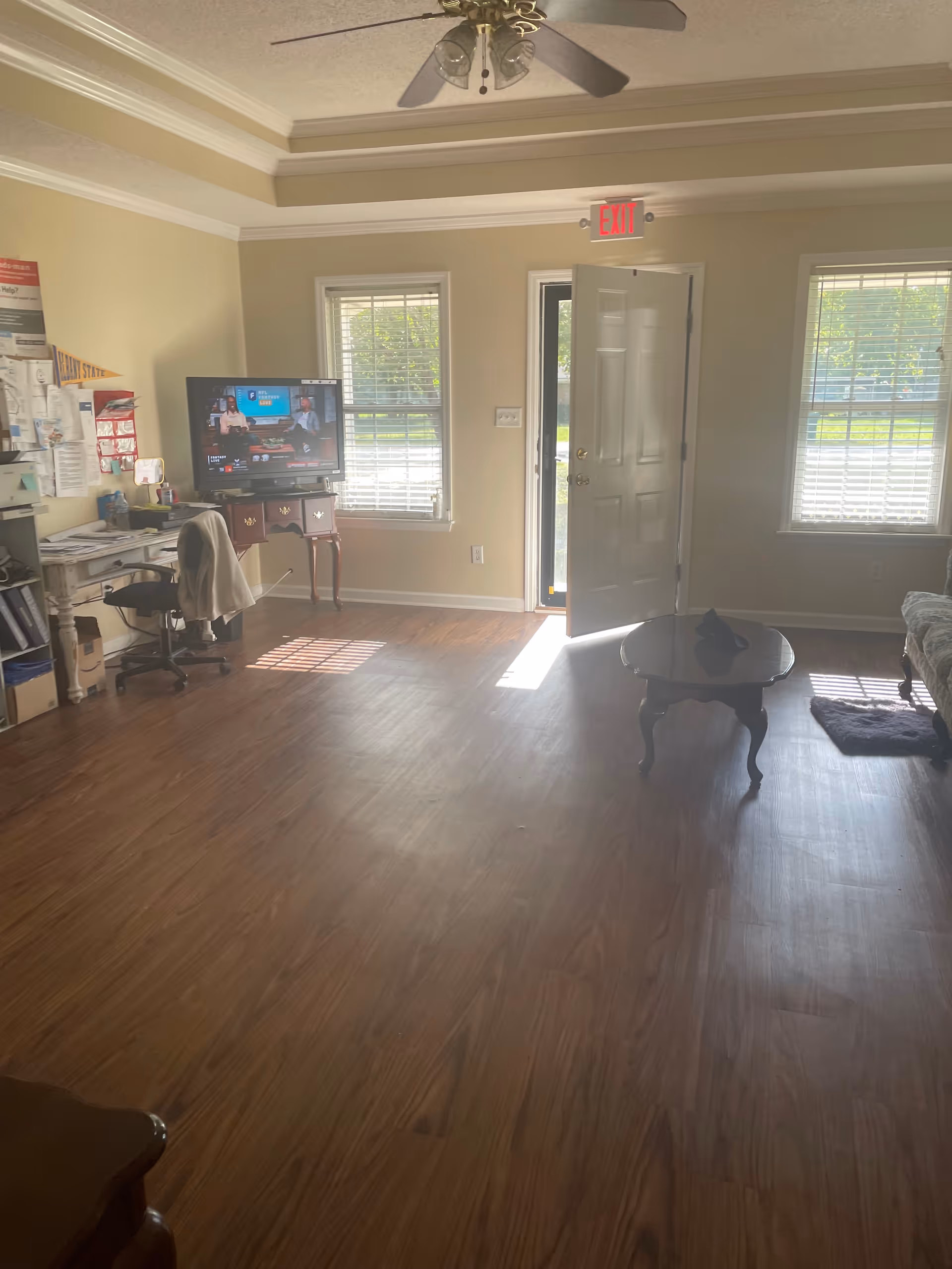 Sunlit living room in Reagan’s Place Personal Care Home with TV, desk, and open door.