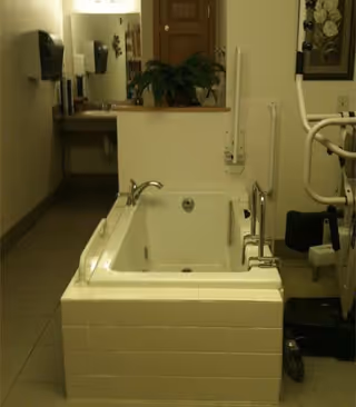 Accessible white tub with grab bars in a senior living facility bathroom.