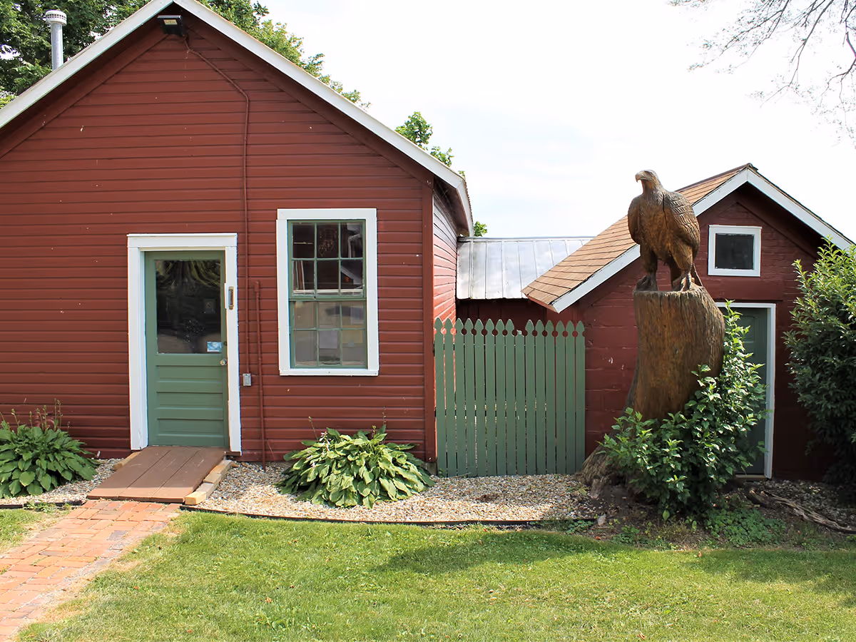 Red wooden building exterior with green door, window, and carved eagle statue.
