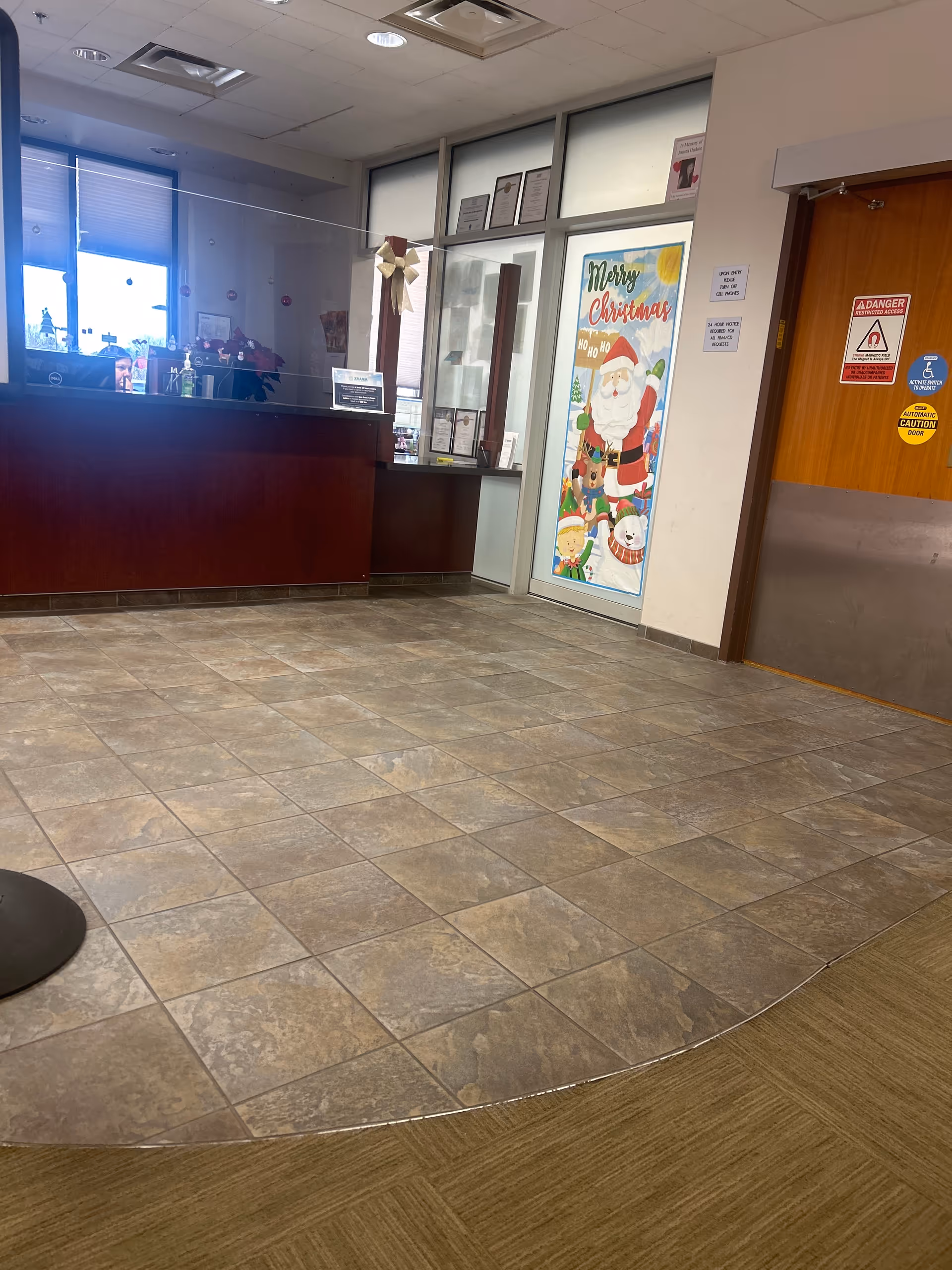Interior reception area with a dark wood front desk, glass partition, and a Merry Christmas door.