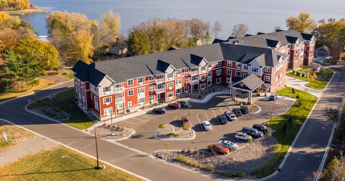 Aerial view of a red-brick senior living building with parking and landscaped grounds.