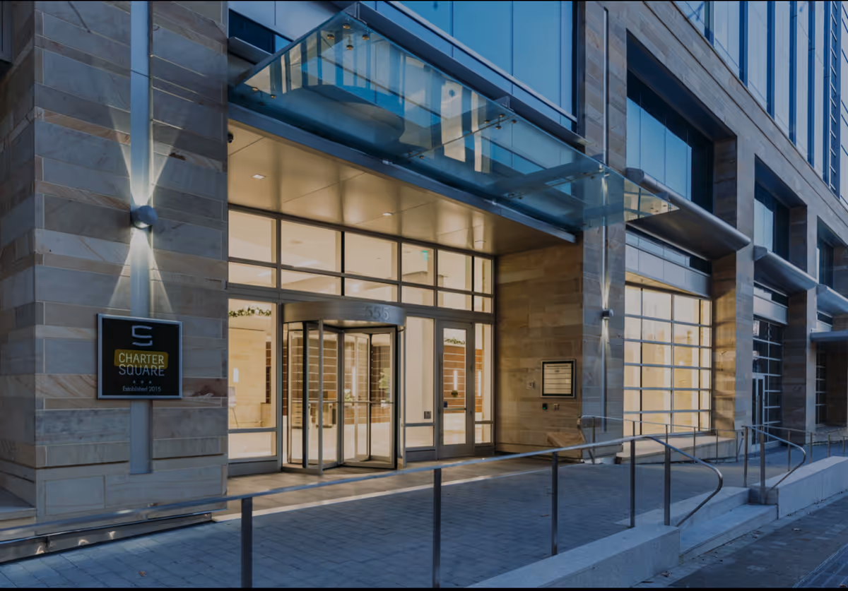 Modern glass-front entrance of a multi-story building with a ramp and walkway.