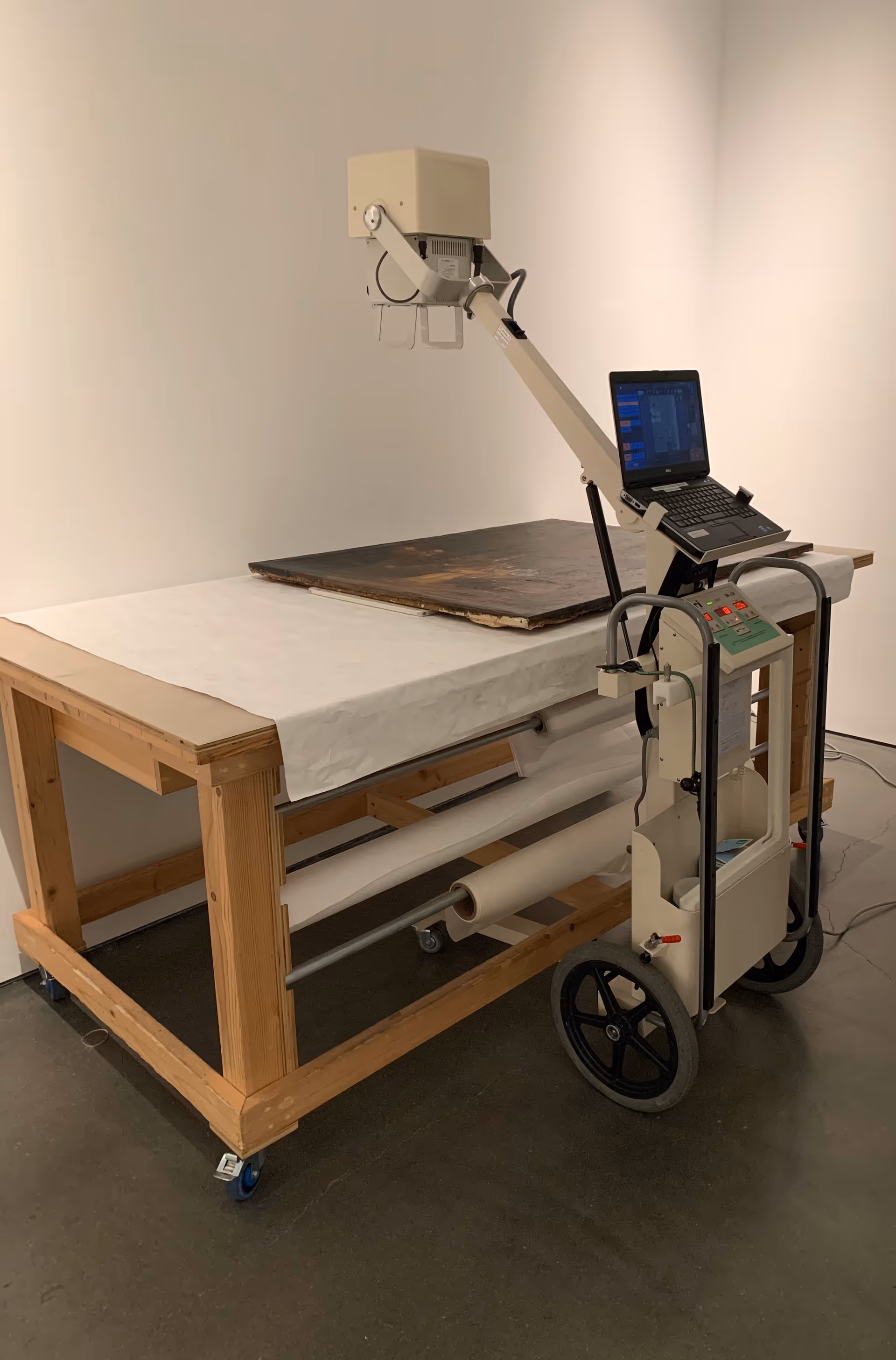 Portable X-ray unit with laptop on a stand beside an exam table in a clinical room.