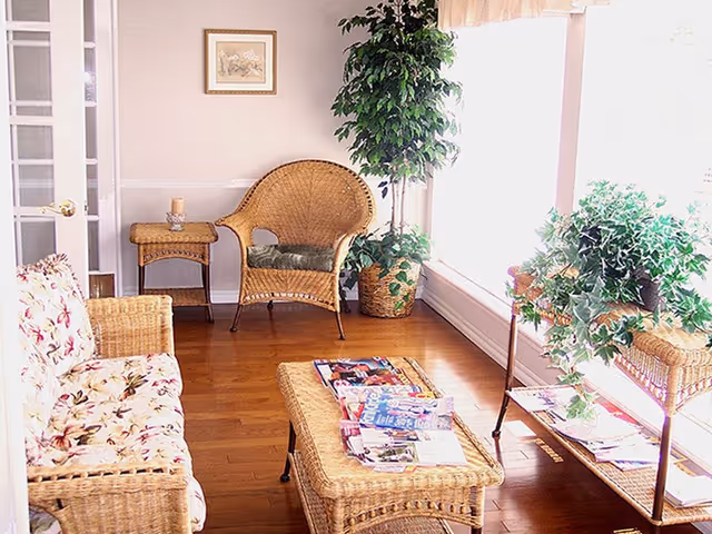 Bright wicker seating area in a sunlit senior living lounge with magazines and plants.
