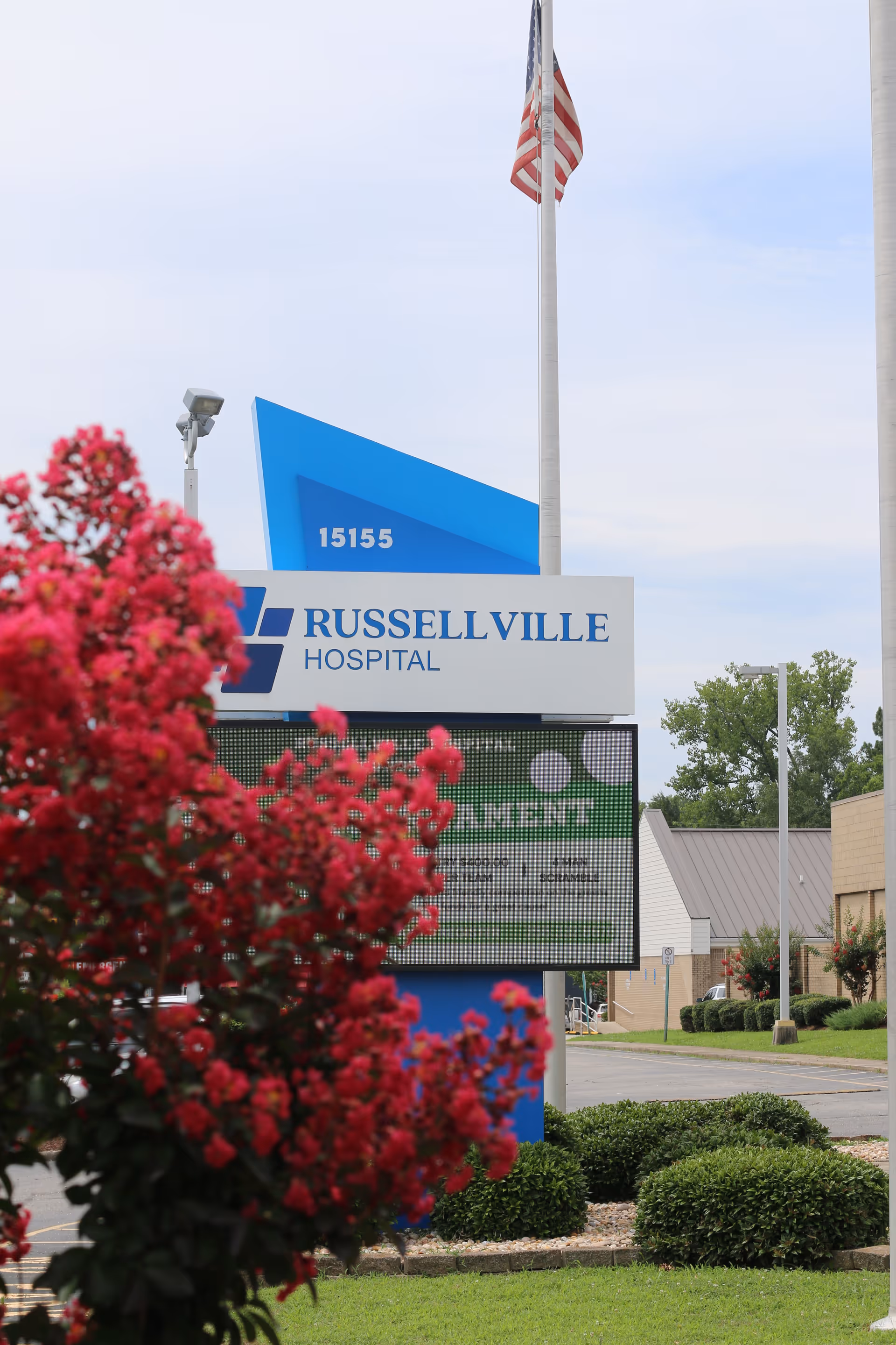 Russellville Hospital sign with flag, blue panels, and blooming pink flowers.
