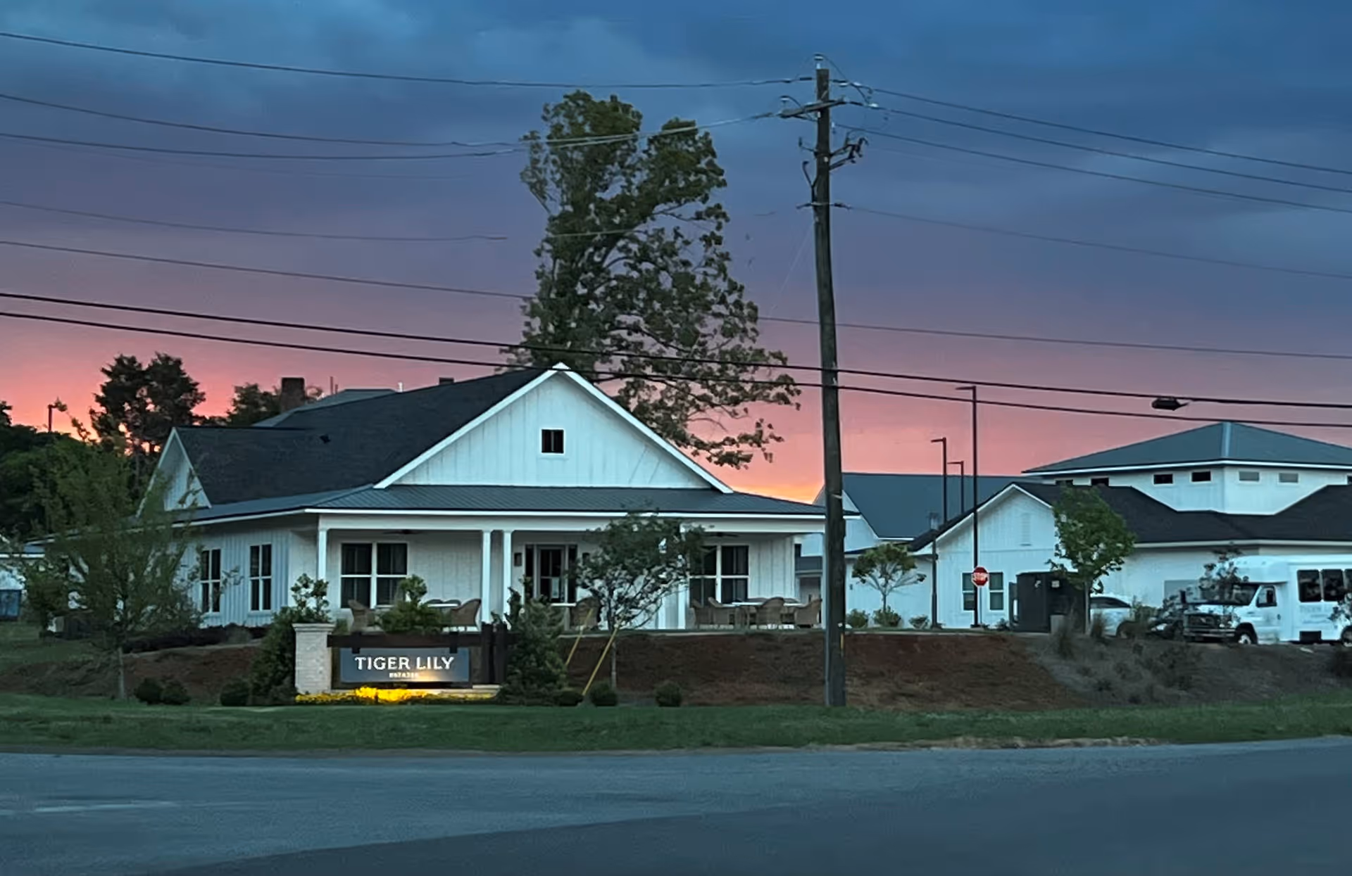Front exterior of Tiger Lily Estates assisted living building at dusk with an illuminated entrance sign and landscaping.