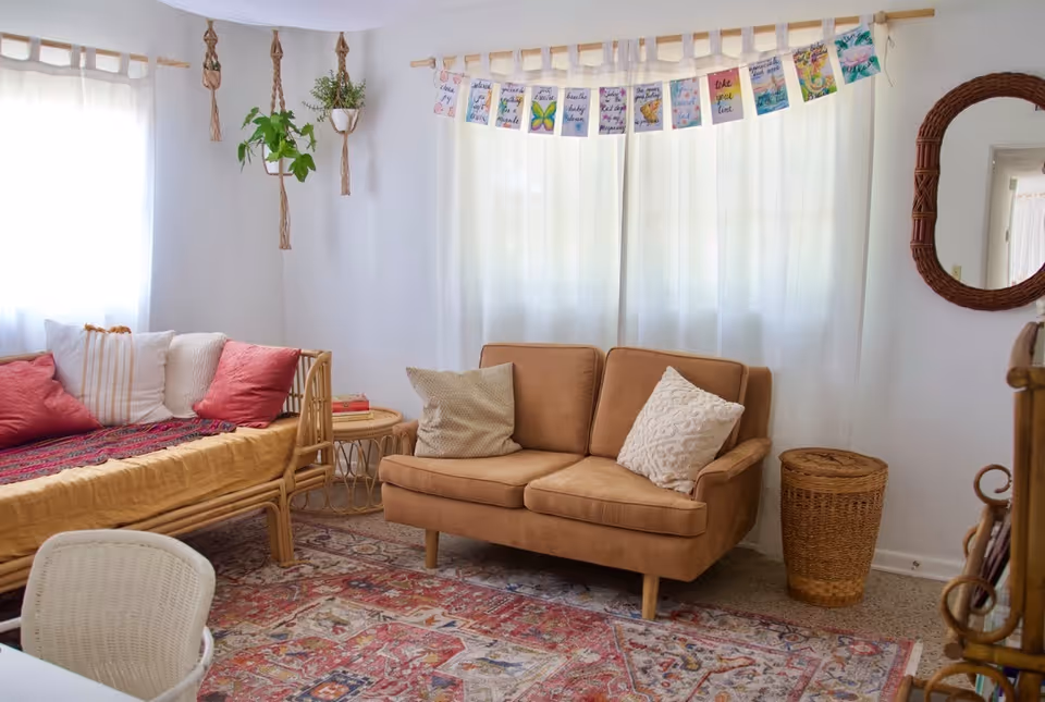 Cozy living room with tan sofa, daybed, plants, and colorful rug.