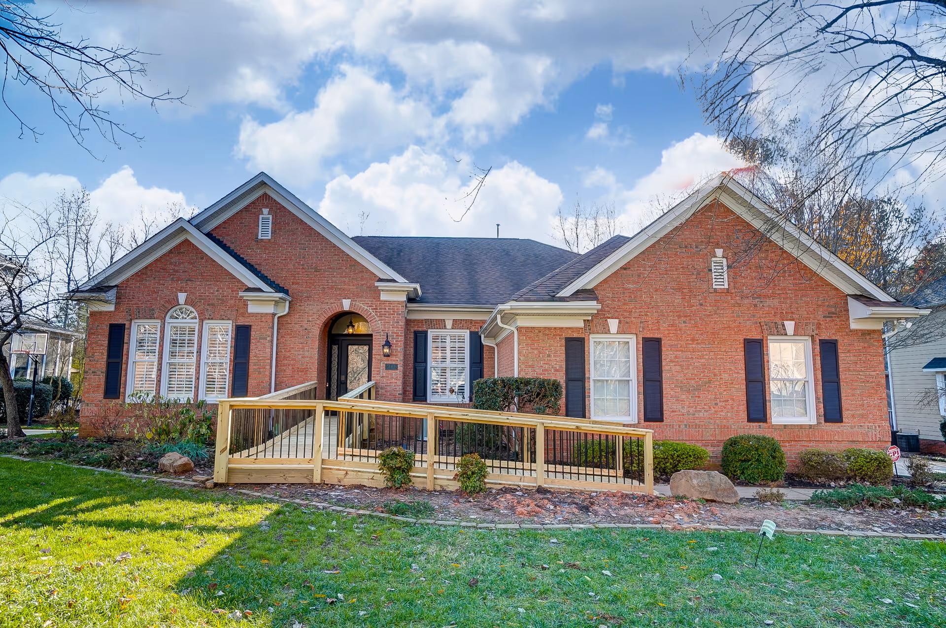 Brick senior living facility with ramped entrance and trimmed shrubs.