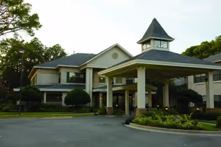 Front view of a two-story senior living facility with a covered porte-cochère, cupola, and landscaped circular driveway.