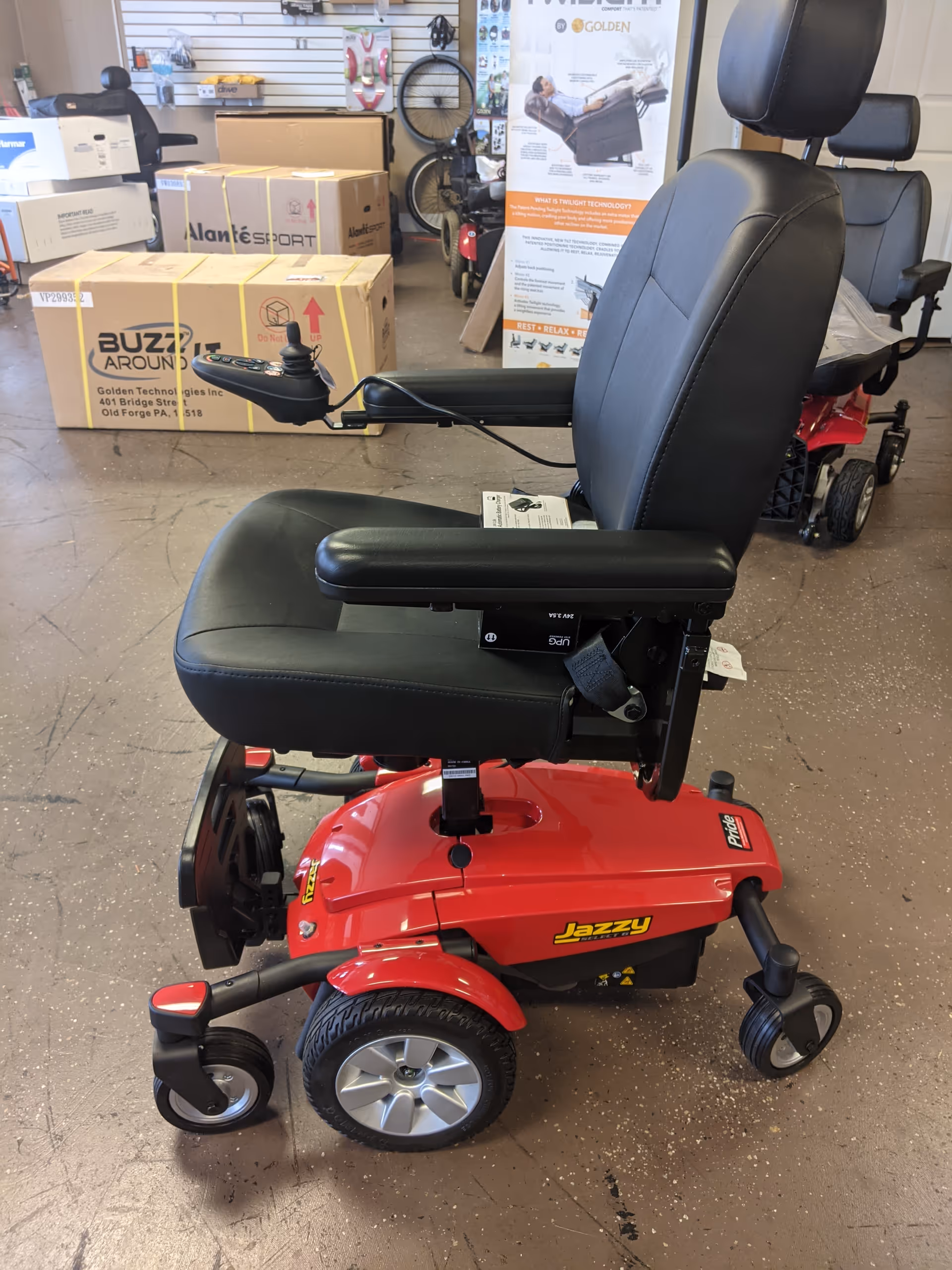 Red Jazzy mobility scooter with armrests in a showroom amid boxes and posters.