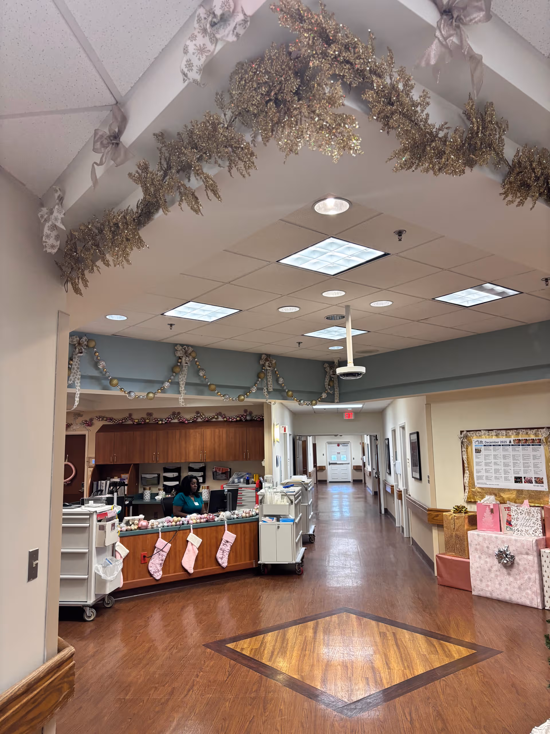 Inside a senior living facility hallway with front desk, garlands, stockings, and wrapped gifts