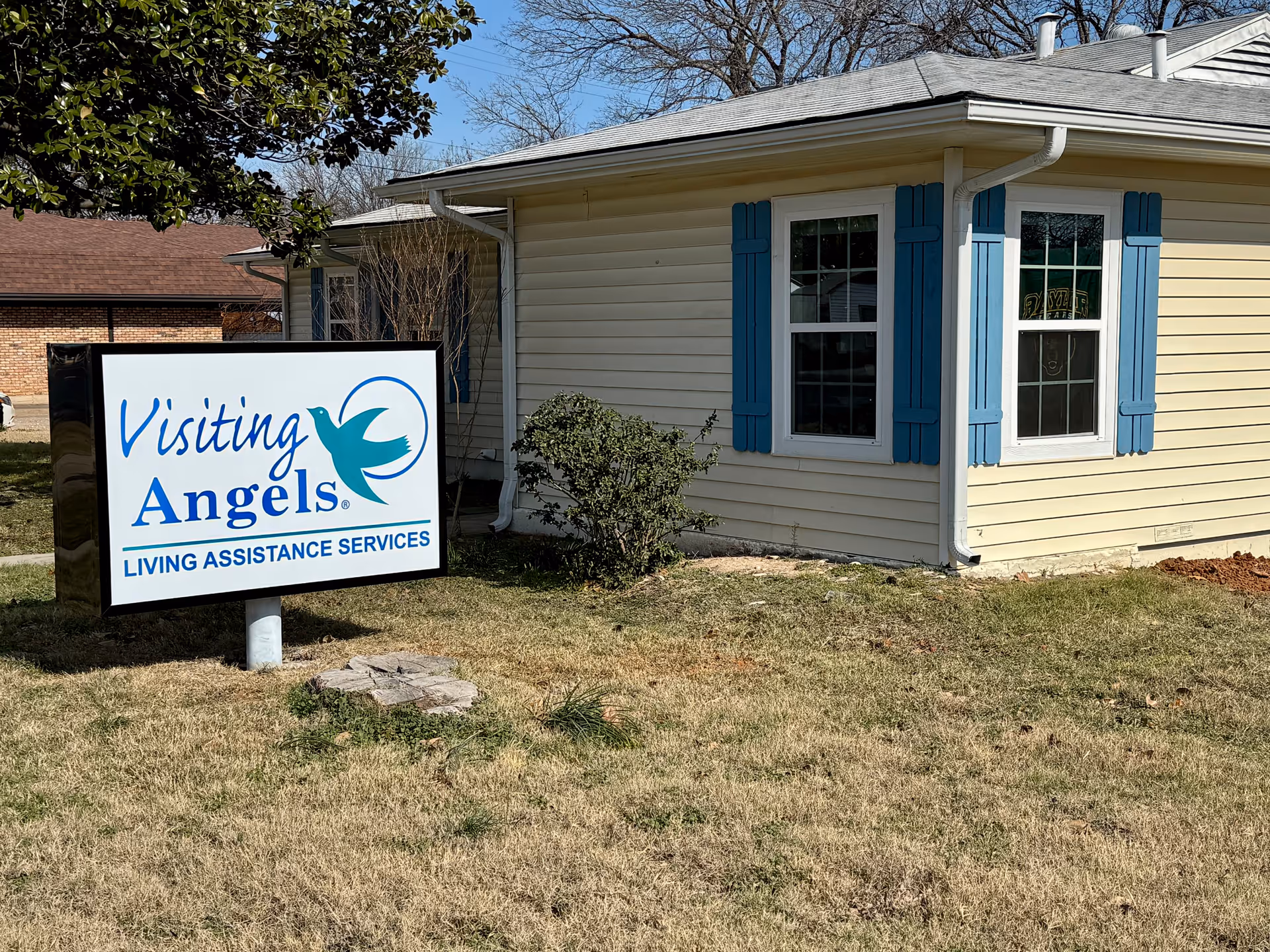 Small one-story building with blue shutters and a Visiting Angels sign in the front yard