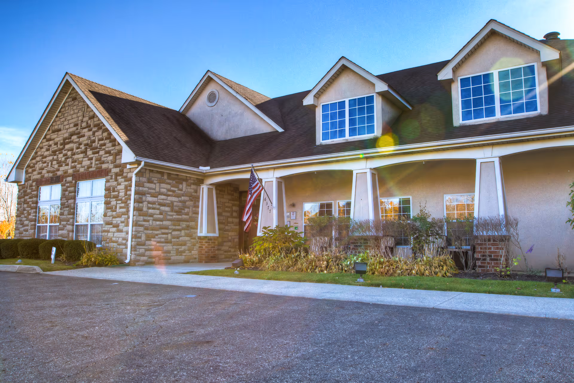Front exterior of a stone-and-siding senior living building with an American flag.