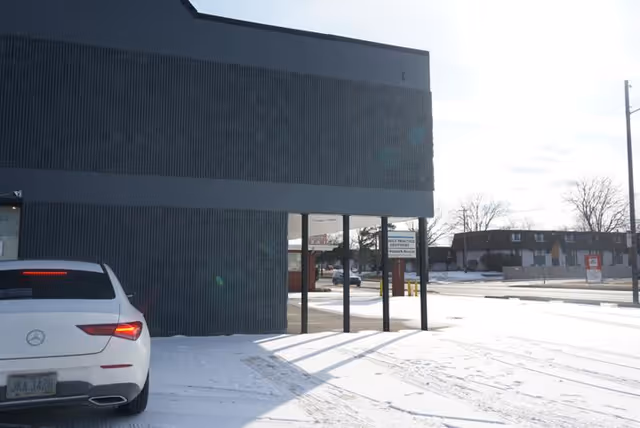 Snowy exterior of a modern building with a parked white Mercedes near the entrance.