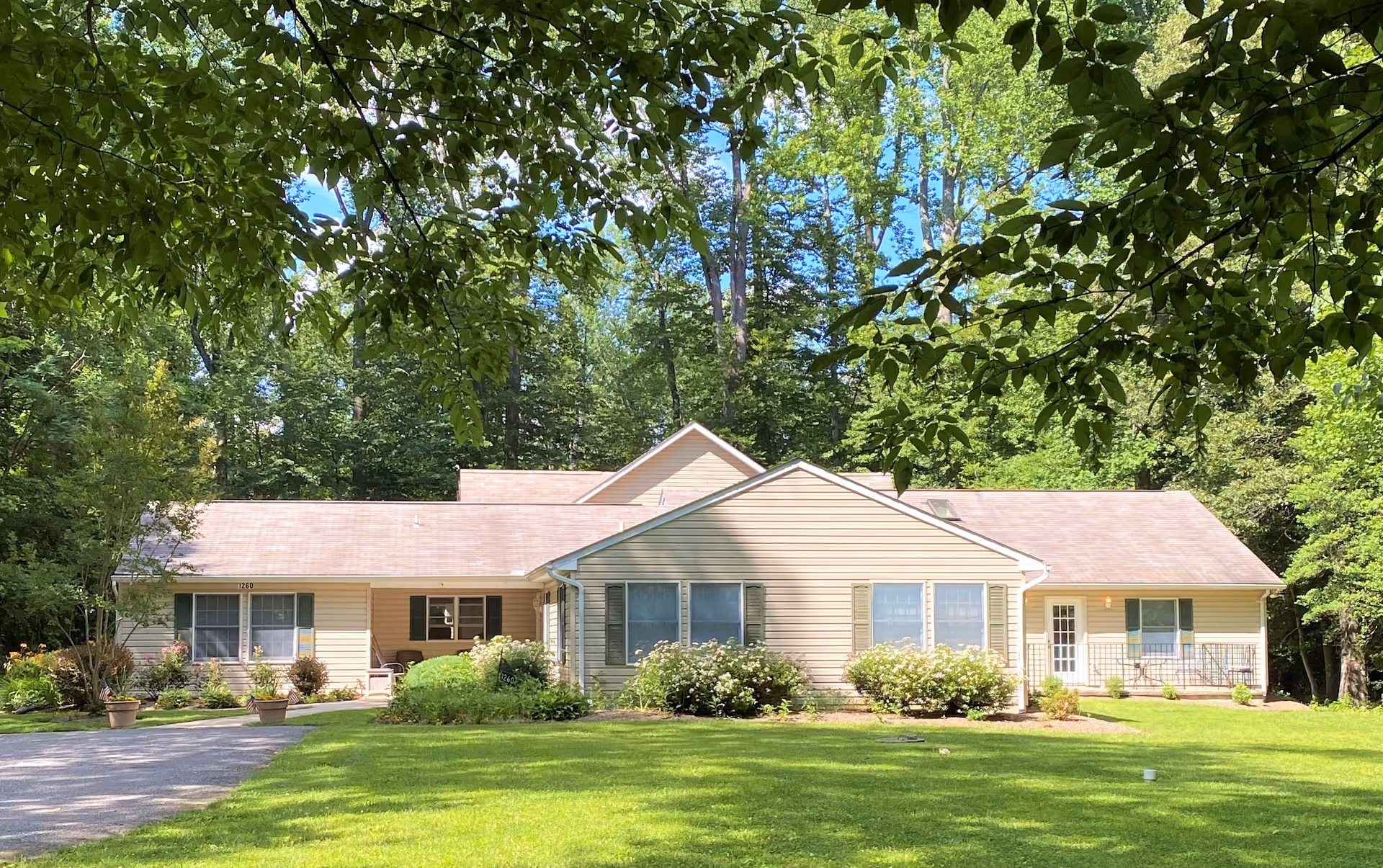 Single-story beige building surrounded by lawn and trees, photographed from the front with leafy branches framing the top.