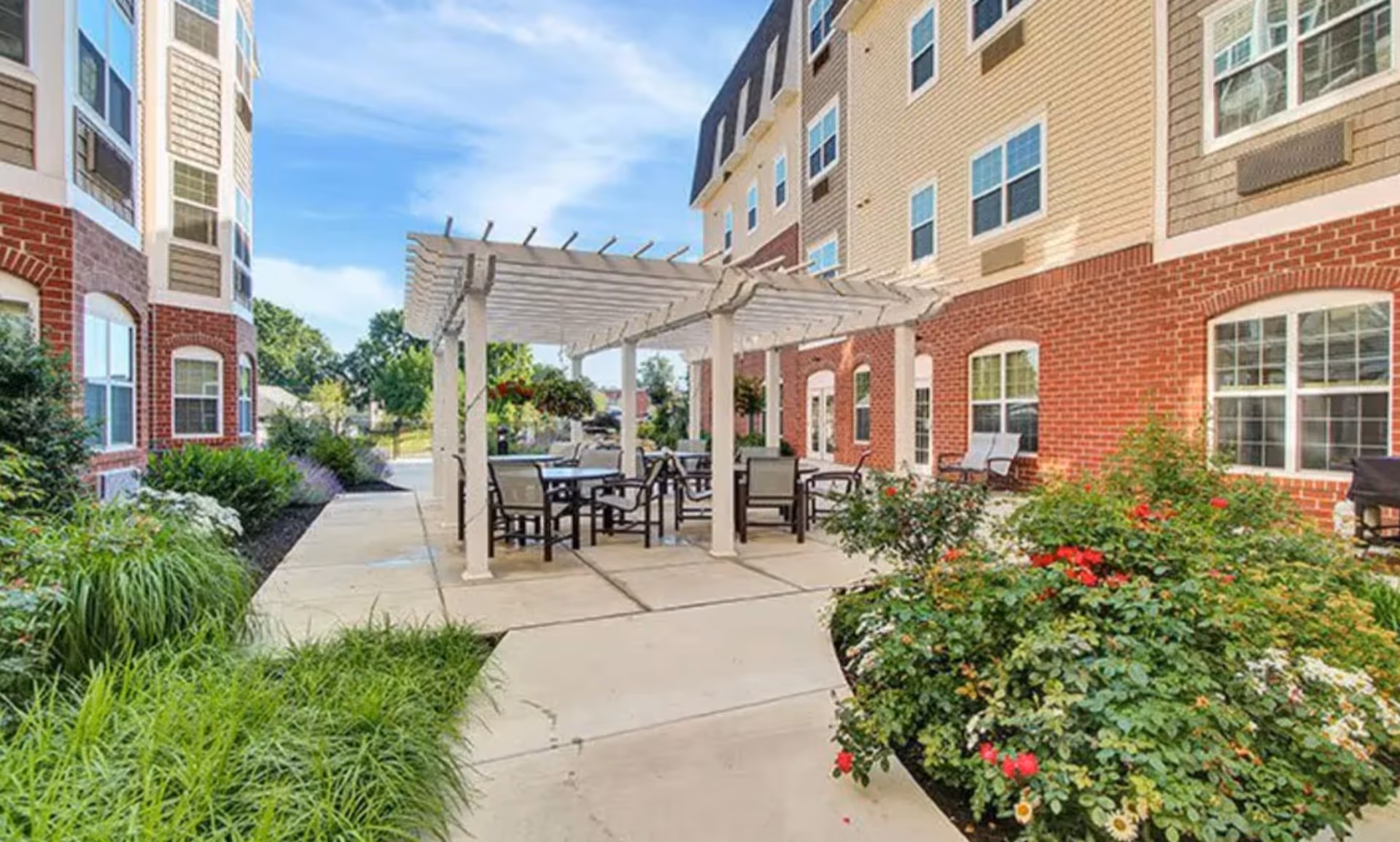 Outdoor patio with a pergola and tables beside a brick senior living building.