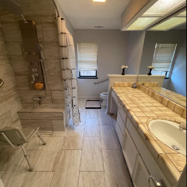 Modern senior living bathroom with tiled shower, seating, and double sinks.
