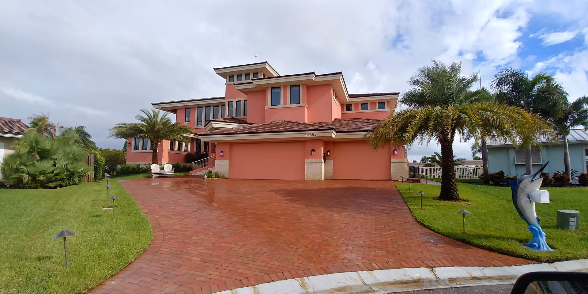 Pink multi-story senior living facility with brick driveway and palm trees in front.